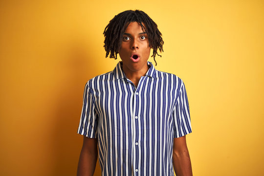Afro man with dreadlocks wearing casual striped t-shirt over isolated yellow background afraid and shocked with surprise expression, fear and excited face.