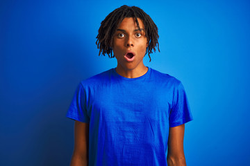 Fototapeta na wymiar Afro american man with dreadlocks wearing t-shirt standing over isolated blue background afraid and shocked with surprise expression, fear and excited face.