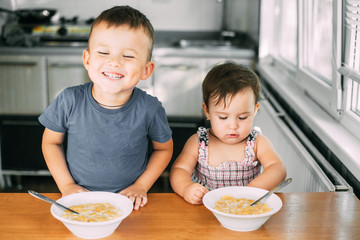 Brother and sister eat cornflakes with milk in the kitchen during the day very fun and cute, dirty...