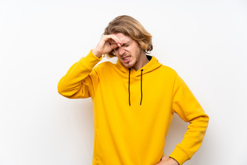 Blonde man with  sweatshirt over white wall with tired and sick expression