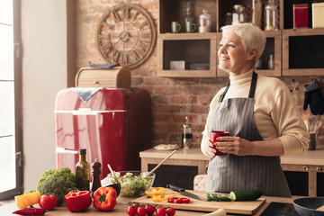 Pensive retired lady enjoying coffee break at kitchen