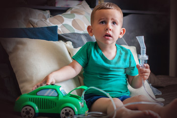 Three year old boy making inhalation with nebulizer at home.