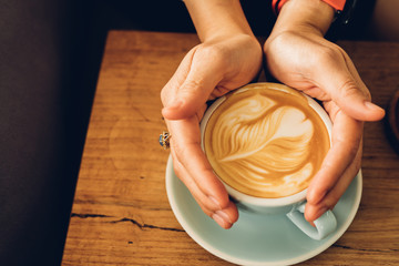Woman hands holding cup of coffee latte in coffee shop.Beautiful foam,ceramic cups, place for text.