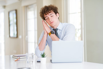 Young business man working with computer laptop at the office sleeping tired dreaming and posing with hands together while smiling with closed eyes.