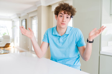 Young handsome man wearing casual blue t-shirt at home clueless and confused expression with arms...