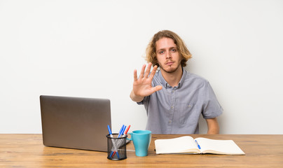 Blonde man with a laptop making stop gesture