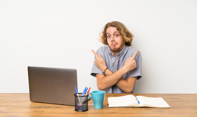 Blonde man with a laptop pointing to the laterals having doubts