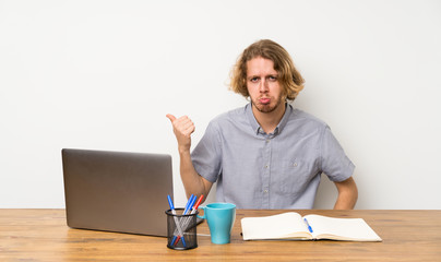 Blonde man with a laptop unhappy and pointing to the side