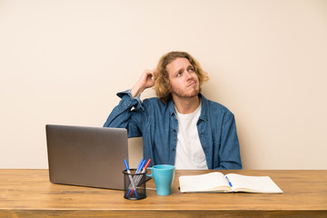 Blonde man with a laptop having doubts and with confuse face expression