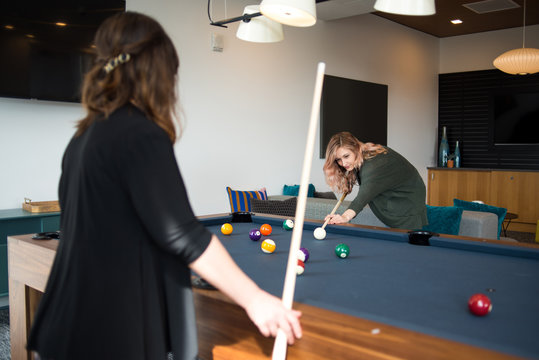 Woman lining up pool shot while friend watches