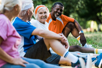 Fototapeta premium selective focus of happy multicultural men and women in sportswear sitting on fitness mats