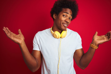 Young african american man listening to music using headphones over isolated red background...