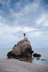The guy climbed a rock into the sea and raised his arms in a victorious gesture.
