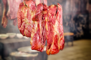 smoked pork meat food on hook in old smokehouse interior on blurry background closeup view of homemade ham traditional gourmet organic beef meal in smoke retro restaurant indoor scene