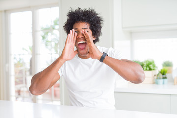 Young african american man wearing casual white t-shirt sitting at home Smiling cheerful playing peek a boo with hands showing face. Surprised and exited