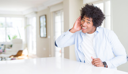 African American man at home smiling with hand over ear listening an hearing to rumor or gossip. Deafness concept.