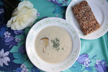 Cream soup of mushrooms in white pot with bread and rose on colorful background