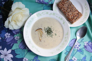Cream soup of mushrooms in white pot with bread and rose on colorful background