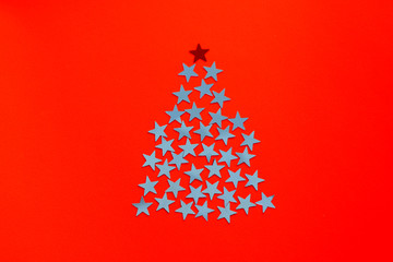 Stars shine in the form Christmas tree silhouette on red background. Minimal composition with copy...