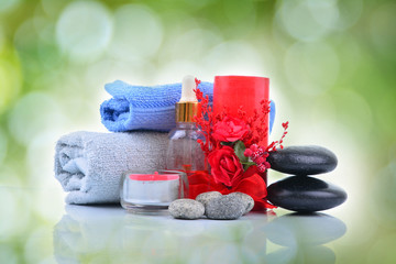 Obraz na płótnie Canvas Red romantic candle and spa oil with towel and zen stone over green blur bokeh background