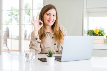 Beautiful young woman using computer laptop doing ok sign with fingers, excellent symbol