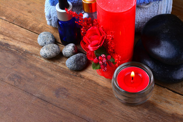 Obraz na płótnie Canvas Red romantic candle and spa oil with towel and zen stone on wooden table