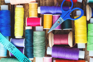 Colored spools of thread laid out in rows on wooden background.