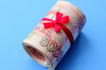 Russian money 5000 rubles twisted into a tube and tied with a ribbon, on a colored background