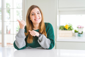 Young beautiful plus size woman wearing casual striped sweater Pointing to the back behind with hand and thumbs up, smiling confident