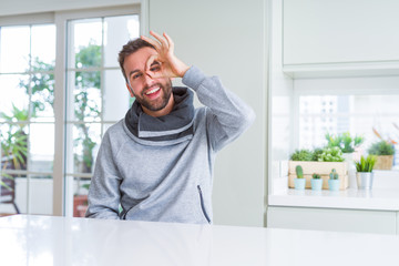 Handsome man at home doing ok gesture with hand smiling, eye looking through fingers with happy face.