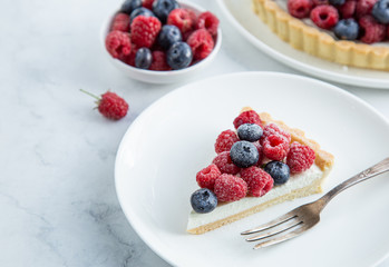 slice of blueberry  and raspberry tart  on white marble background