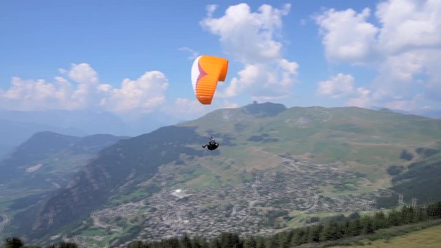 Two extreme paragliders flying in the distance against a clear blue sky in Switzerland. Adventurers in the sky over the Alps. People fly in the sky. Two paratroopers soar above the villages. Hobbies 