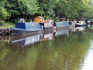 Obraz premium narrow boats and barges moored on the rochdale canal in hebden bridge surrounded by green summer trees and a stone footbridge