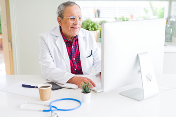 Obraz premium Senior doctor man at the clinic working with computer and smiling