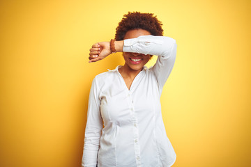 African american business woman over isolated yellow background covering eyes with arm smiling cheerful and funny. Blind concept.