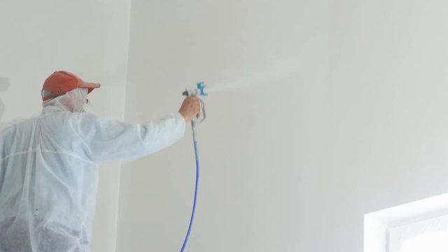repair of the apartment - professional painter paints the walls with white paint spray gun