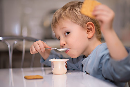 Adorable little blonde boy eating yogurt with a spoon