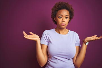 Young beautiful african american woman with afro hair over isolated purple background clueless and...
