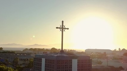 Aerial shot of modern church at sunset in the city. Cross silhouette on top of church steeple. Crucifix with sunlight and urban core landscape of Berkley, California. - Powered by Adobe