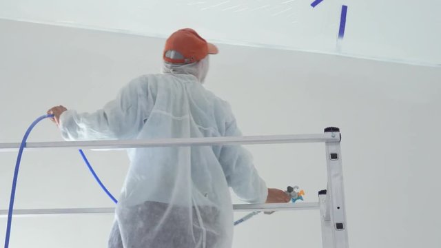 repair of the apartment - professional painter paints the walls with white paint spray gun