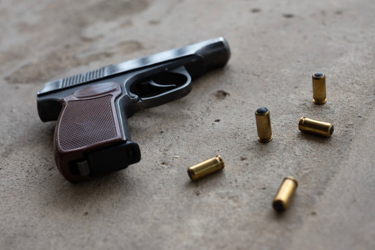 traumatic metal gun with 9 mm bullets on a gray concrete background. side view, flat lay, copy space