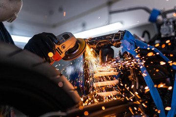 Worker cutting, grinding and polishing motorcycle metal part with sparks indoor workshop, close-up.