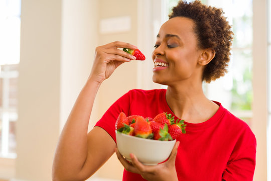 Beautiful young african woman with afro hair eating fresh strawberries