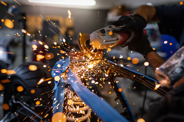 Fototapeta na wymiar Worker cutting, grinding and polishing motorcycle metal part with sparks indoor workshop, close-up.