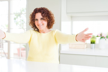 Beautiful senior woman wearing yellow sweater looking at the camera smiling with open arms for hug. Cheerful expression embracing happiness.