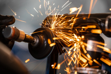 Worker cutting, grinding and polishing motorcycle metal part with sparks indoor workshop, close-up.