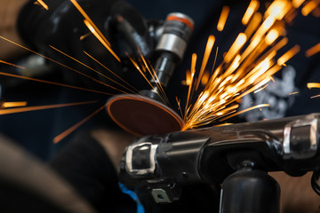 Worker cutting, grinding and polishing motorcycle metal part with sparks indoor workshop, close-up.