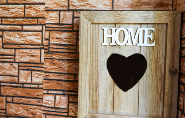 Wooden key box holding on the wall with heart in the middle. Letters Home in white and square tiles at the entrances of the home. Love and home concept.