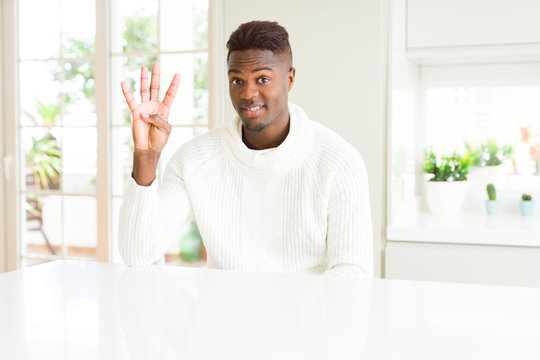 Handsome african american man on white table showing and pointing up with fingers number four while smiling confident and happy.