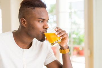 Handsome young african man drinking a glass of fresh natural orange juice enjoying fruit refreshment